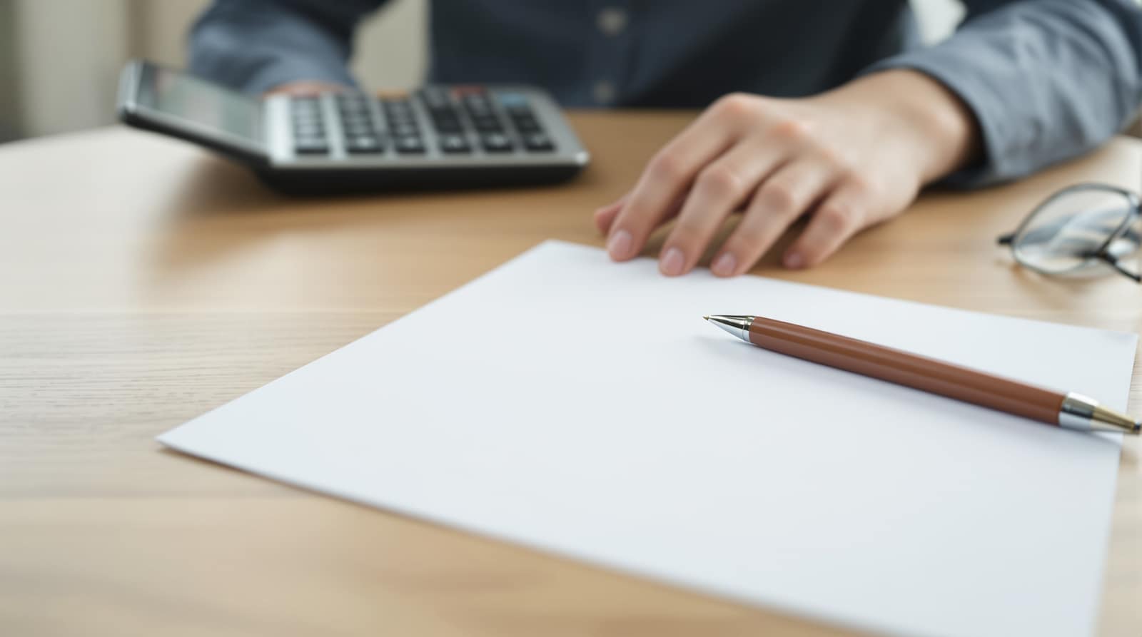 A calculator, a pen, and paperwork on a wooden desk in soft daylight