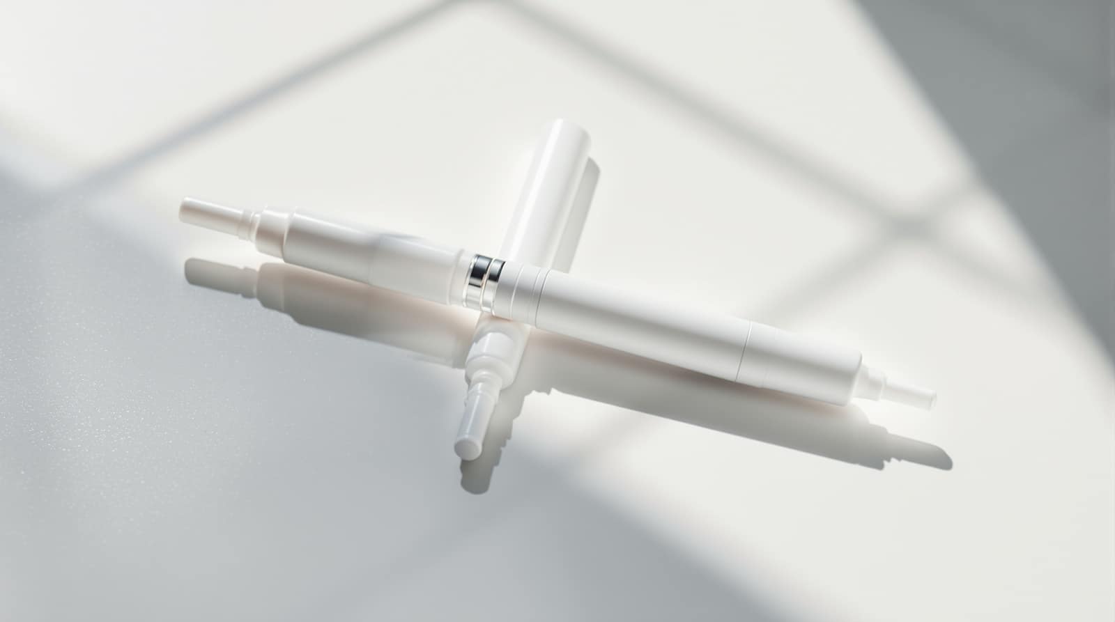 Two unbranded medical injection pens side by side on a clean white clinical surface in soft daylight